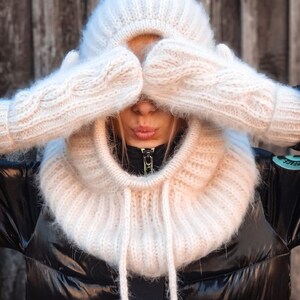 Pu&ograve; includere: Un collo a lupetto di maglia bianca con cappello e guanti abbinati. Il collo a lupetto ha una lunga cravatta che pu&ograve; essere indossata davanti o dietro.