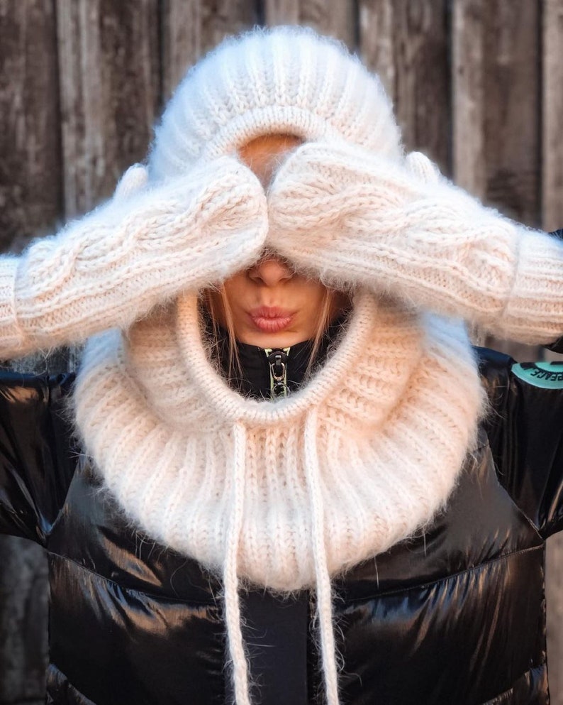 Pu&ograve; includere: Un collo a lupetto di maglia bianca con cappello e guanti abbinati. Il collo a lupetto ha una lunga cravatta che pu&ograve; essere indossata davanti o dietro.