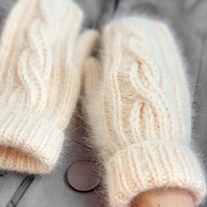 Pu&ograve; includere: Un paio di guanti senza dita di colore crema a maglia con un motivo a treccia. I guanti hanno una consistenza soffice e sono realizzati con un filato morbido.
