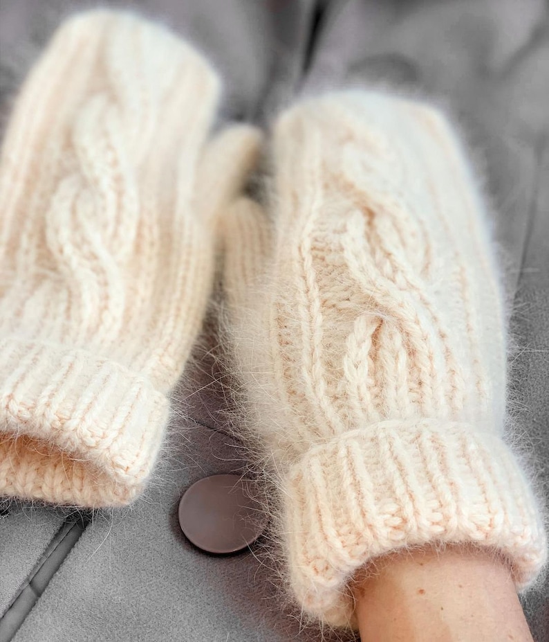 Pu&ograve; includere: Un paio di guanti senza dita di colore crema a maglia con un motivo a treccia. I guanti hanno una consistenza soffice e sono realizzati con un filato morbido.