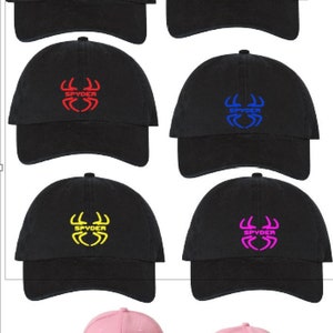 May include: Six black baseball caps with a spider logo in different colors: white, green, red, blue, yellow, and pink. One pink baseball cap with a black spider logo.