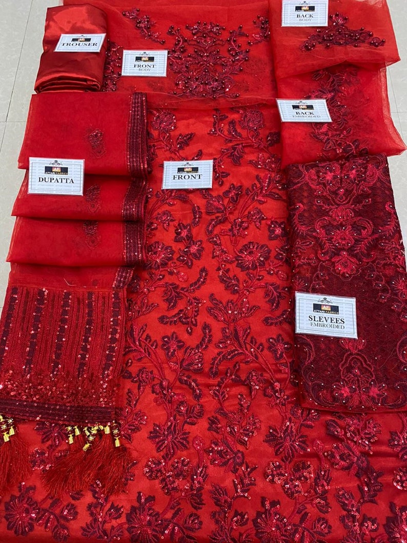 May include: A vibrant red embroidered fabric set, including a dupatta, trousers, and front and back panels. The fabric is adorned with intricate floral patterns and sequins. The set also includes embroidered sleeves. The labels read "FRONT", "BACK", "SLEEVES EMBROIDERED", "TROUSER", and "DUPATTA".