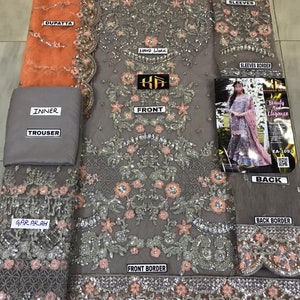 以下が含まれることがあります： グレーの刺繍が施されたフォーマルな衣装で、複雑な花柄とスパンコールのディテールが特徴です。 セットには、デュパッタ、インナーライニング、ズボン、そして「手作業」と「袖」の詳細が記載された「フロント」とラベル付けされた衣服が含まれています。 デザインは、タッセル付きのスカラップボーダーが特徴です。