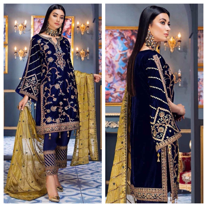 May include: A two-piece navy blue velvet outfit with gold embroidery. The long-sleeved top features floral and geometric patterns, and the matching pants have a similar design. A gold-colored scarf completes the ensemble.
