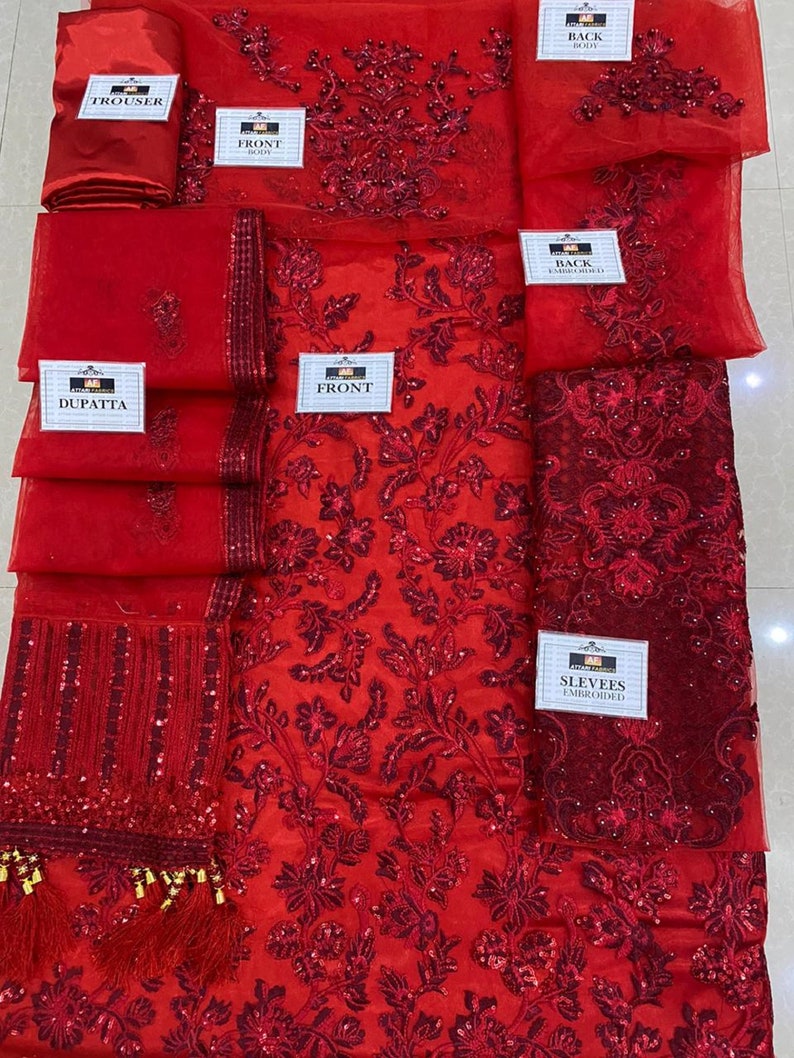May include: A red embroidered fabric set, including a trouser, dupatta, and various panels labeled "front," "back," and "sleeves." The fabric features intricate floral patterns and embellishments.