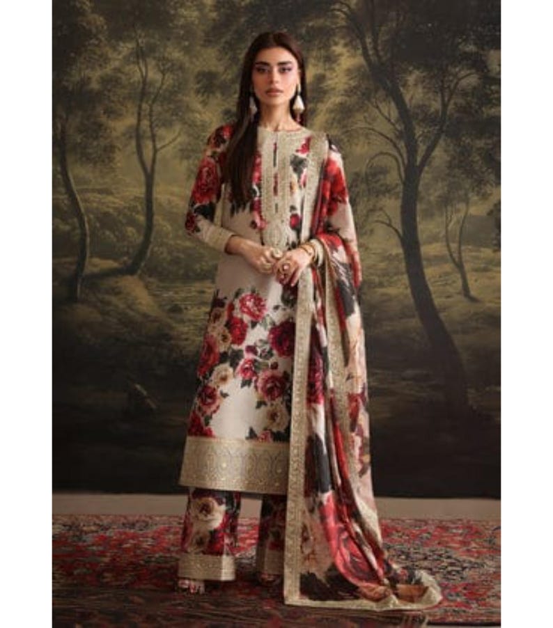 Puede incluir: Un conjunto con estampado floral crema que presenta una t&uacute;nica de manga larga, pantalones a juego y una bufanda drapeada. El estampado floral incluye rosas rojas y rosas. El ribete dorado acent&uacute;a los bordes del atuendo. El atuendo lo lleva una persona.