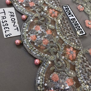 以下が含まれることがあります： 精巧な花柄刺繍が施された装飾布のクローズアップ。デザインは、シルバーのスパンコール、ピーチ色の花、ピンクのパールのような装飾が特徴です。「FRONT BORDER」と「FRONT TASSELS」の文字が見えます。
