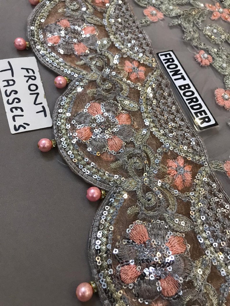 以下が含まれることがあります： 精巧な花柄刺繍が施された装飾布のクローズアップ。デザインは、シルバーのスパンコール、ピーチ色の花、ピンクのパールのような装飾が特徴です。「FRONT BORDER」と「FRONT TASSELS」の文字が見えます。