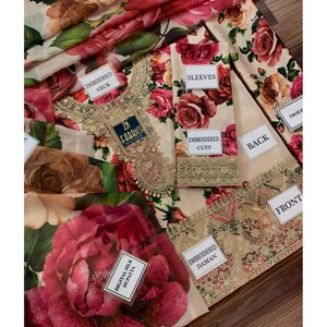 Puede incluir: Un conjunto de tela con estampados florales y etiquetas que indican "Embroidered Neck", "Sleeves", "Embroidered Cuff", "Back", "Front" y "Embroidered Daman". El dise&ntilde;o presenta grandes rosas rojas y rosas sobre un fondo crema.
