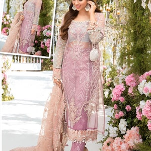 May include: A sheer, light purple formal dress with intricate embroidery and long sleeves. The dress features a matching scarf and is paired with light pink heels. The background includes pink and white flowers and decorative lighting.