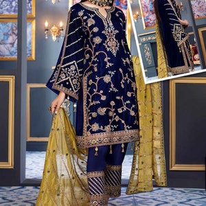 May include: A navy blue velvet embroidered outfit with gold accents. The ensemble includes a long-sleeved tunic, matching pants, and a sheer gold scarf. The tunic features intricate floral embroidery and a flared sleeve design. The pants have embroidered cuffs.