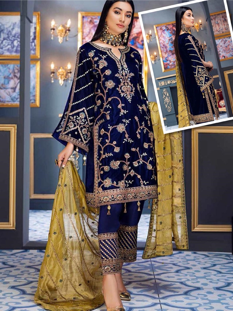 May include: A navy blue velvet embroidered outfit with gold accents. The ensemble includes a long-sleeved tunic, matching pants, and a sheer gold scarf. The tunic features intricate floral embroidery and a flared sleeve design. The pants have embroidered cuffs.