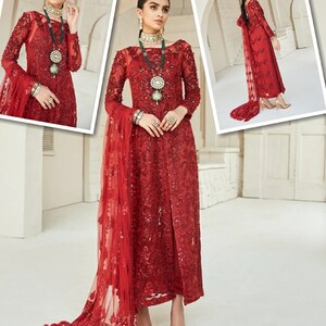May include: A red, long-sleeved formal dress with intricate embroidery and a flowing train. The dress features a high neckline and is adorned with embellishments. The ensemble includes a matching sheer scarf. The model is wearing jewelry and heels.