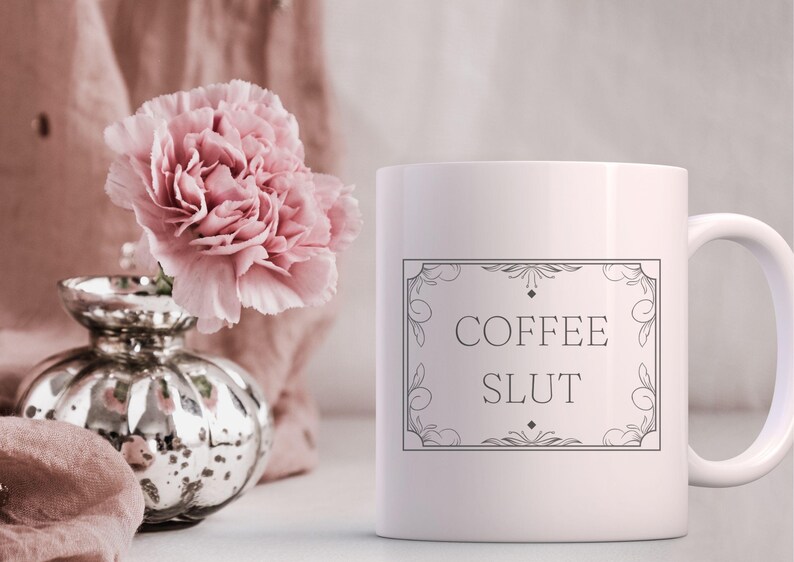Pu&ograve; includere: Tazza da caff&egrave; in ceramica bianca con un contorno nero di una cornice decorativa e il testo "COFFEE SLUT" all'interno della cornice.