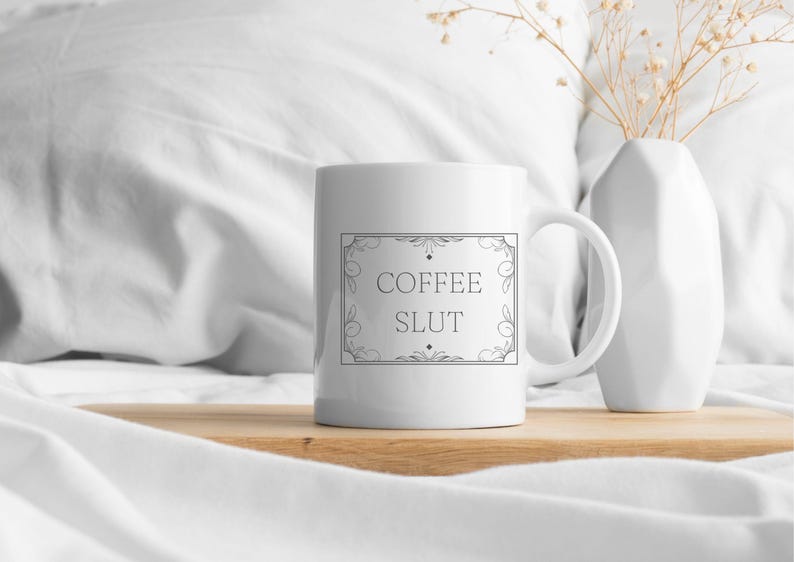 Pu&ograve; includere: Tazza da caff&egrave; in ceramica bianca con un contorno nero di una cornice decorativa e il testo "COFFEE SLUT" all'interno della cornice.