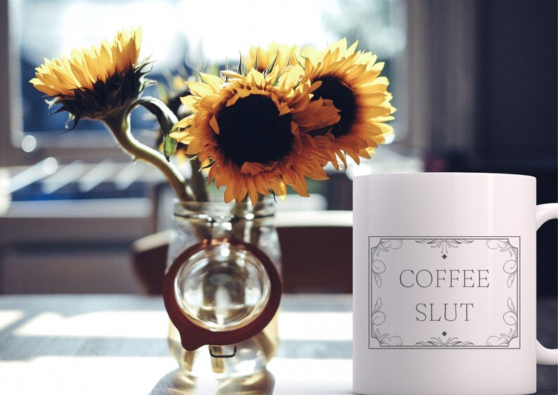 Pu&ograve; includere: Una tazza da caff&egrave; in ceramica bianca con un contorno nero di una cornice decorativa e il testo "COFFEE SLUT" all'interno. La tazza &egrave; appoggiata su una superficie bianca con un mazzo di girasoli in un barattolo di vetro.