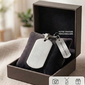 Peut inclure: Un pendentif en forme de plaque d'identité argenté et rectangulaire, accompagné d'une petite étiquette, présentés dans un coffret marron. La petite étiquette mesure 36mm x 22mm. Le coffret affiche le texte "KINGRAVURE" et "Éternisez Vos Moments les Plus Précieux".
