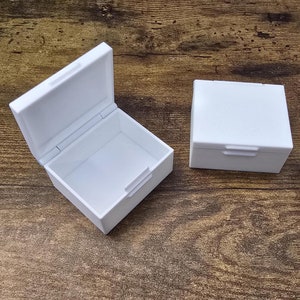May include: Three white plastic boxes with hinged lids. The boxes are square and have a simple design.