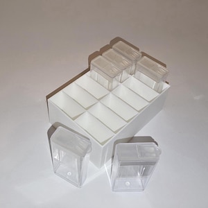 May include: A white, compartmentalised organiser with clear plastic containers. The organiser has multiple square compartments, each designed to hold a small container. Three clear containers are outside the organiser. The containers have clear lids.