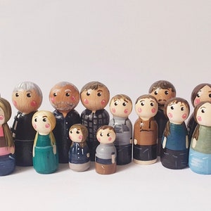 May include: A set of 15 wooden peg dolls, painted in various colors and designs, representing a family. The dolls are standing in a row on a white background.
