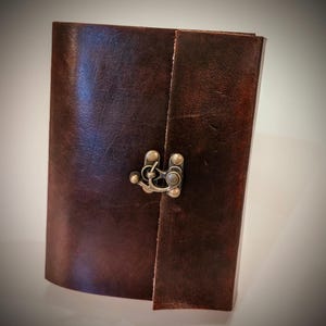 May include: A brown leather journal with a metal clasp. The journal has a distressed look and is closed.