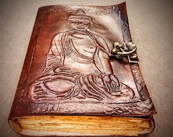 Könnte beinhalten: Ein braunes Lederjournal mit einem detaillierten, geprägten Bild von Buddha auf dem vorderen Umschlag. Das Journal hat einen Verschluss aus Messing.