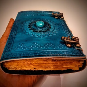 Peut inclure: Un journal relié en cuir turquoise avec un incrustation de pierre turquoise et des fermoirs métalliques ornés. Le journal a un aspect vieilli et est ouvert pour révéler des pages vierges.