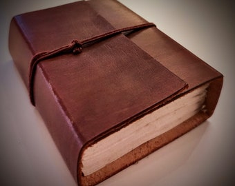 May include: A brown leather-bound journal with a string closure. The journal is closed and the string is tied around it.