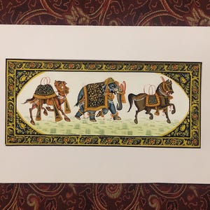 May include: An Indian miniature painting featuring a camel, an elephant, and a horse, all adorned with ornate coverings. The animals are depicted in a line, set against a light green background within a decorative frame.