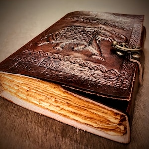 May include: A brown leather journal with an embossed elephant design and a metal clasp. The journal has a worn, vintage look and is closed.