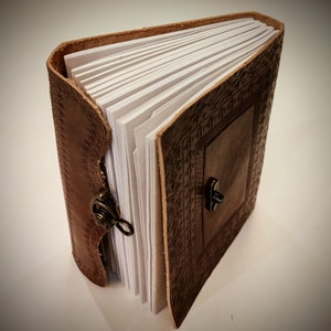 May include: A brown leather-bound journal with a decorative embossed design and a brass clasp. The journal is open to reveal blank pages.