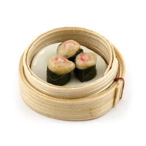 Könnte beinhalten: Drei gedämpfte Brötchen in einem Bambus-Dampfgarer. Die Brötchen sind mit einer weißen Füllung gefüllt und mit einer rosa Zutat belegt.