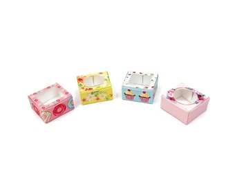 May include: Four small, square boxes with clear windows. The boxes are decorated with different patterns, including donuts, flowers, and cupcakes. The boxes are made of cardboard and are perfect for packaging small gifts or favors.