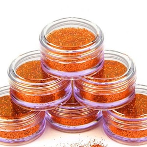 Op de afbeelding: Zes kleine, doorzichtige potjes gevuld met oranje glitter. De potjes zijn in een piramidevorm gestapeld.