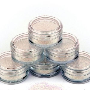 May include: Six small round jars of iridescent glitter, stacked in a pyramid shape. The jars are clear plastic with silver lids.