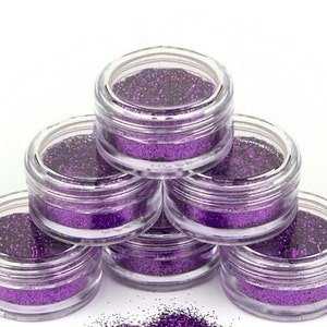 Peut inclure: Six petits pots transparents remplis de paillettes violettes, empilés en forme de pyramide.
