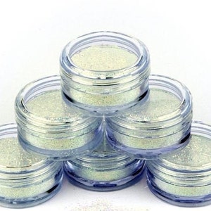 Op de afbeelding: Zes kleine, doorzichtige potjes gevuld met iriserende glitter. De potjes zijn in een piramidevorm gestapeld.