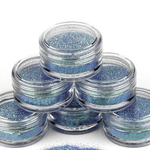 Op de afbeelding: Zes kleine, doorzichtige potjes gevuld met blauwe glitter. De potjes zijn in een piramidevorm gestapeld.