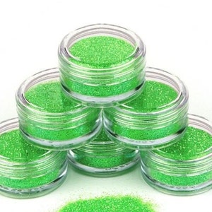 Op de afbeelding: Zes kleine, doorzichtige potjes gevuld met felgroene glitter. De potjes zijn in een piramidevorm gestapeld.