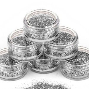 Op de afbeelding: Zes kleine, doorzichtige potjes gevuld met zilveren glitter. De potjes zijn in een piramidevorm gestapeld.