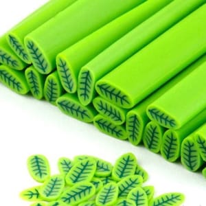 Puede incluir: Una colección de canes de arcilla polimérica verde con un diseño de hojas. Los canes están apilados en una pila y también hay formas de hojas sueltas.