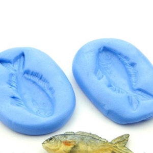 Könnte beinhalten: Zwei hellblaue Silikonformen in ovaler Form, jede mit einem detaillierten Fischdesign. Unten befindet sich ein realistisches Fischmodell. Die Formen sind zum Basteln oder Backen gedacht, perfekt für die Herstellung von fischförmigen Gegenständen.