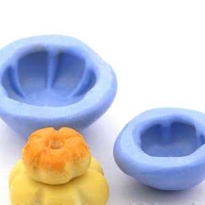 Könnte beinhalten: Zwei blaue Silikonformen zum Backen, eine größere und eine kleinere. Die größere Form ist schalenförmig mit einem geriffelten Rand. Die kleinere Form ist kuppelförmig. Im Vordergrund befindet sich ein Stapel aus drei gelben und orangefarbenen Kuchendekorationen.