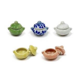 May include: Five miniature ceramic pots with lids. The pots are in various colors, including green, blue, white, yellow, and pink. The lids are all slightly different shapes and sizes.