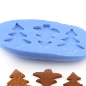 Könnte beinhalten: Eine hellblaue Silikonform mit drei Weihnachtsbaumformen. Unter der Form befinden sich drei gebackene Lebkuchen-Weihnachtsbäume. Die Form ist oval und die Bäume sind detailliert.