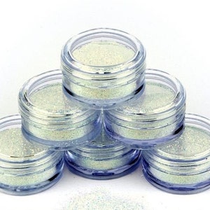 Op de afbeelding: Zes kleine, doorzichtige potjes gevuld met iriserende glitter. De potjes zijn in een piramidevorm gestapeld.