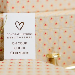 Puede incluir: Una tarjeta blanca con un corazón dorado y el texto "Congratulations & Best Wishes On Your Chuni Ceremony" en una caja estampada.