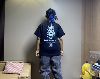 Puede incluir: Una camiseta negra con un gráfico blanco de una calavera con llamas en la espalda. El texto "Roariders Design by Hidden" está impreso debajo del gráfico. La camiseta la lleva puesta una persona con el pelo azul.