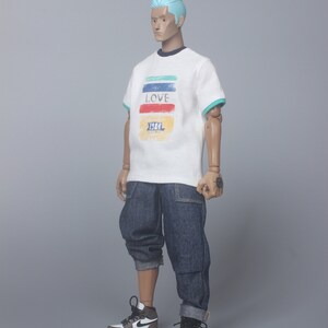May include: A white t-shirt with a colorful striped design and the word "LOVE" printed on the front. The shirt also has the text "1984" printed on the front. The model is wearing blue jeans and white and black sneakers.