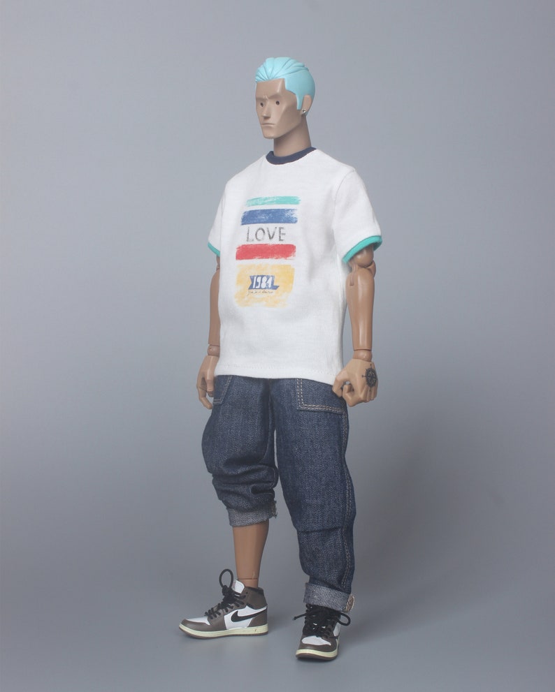 May include: A white t-shirt with a colorful striped design and the word "LOVE" printed on the front. The shirt also has the text "1984" printed on the front. The model is wearing blue jeans and white and black sneakers.